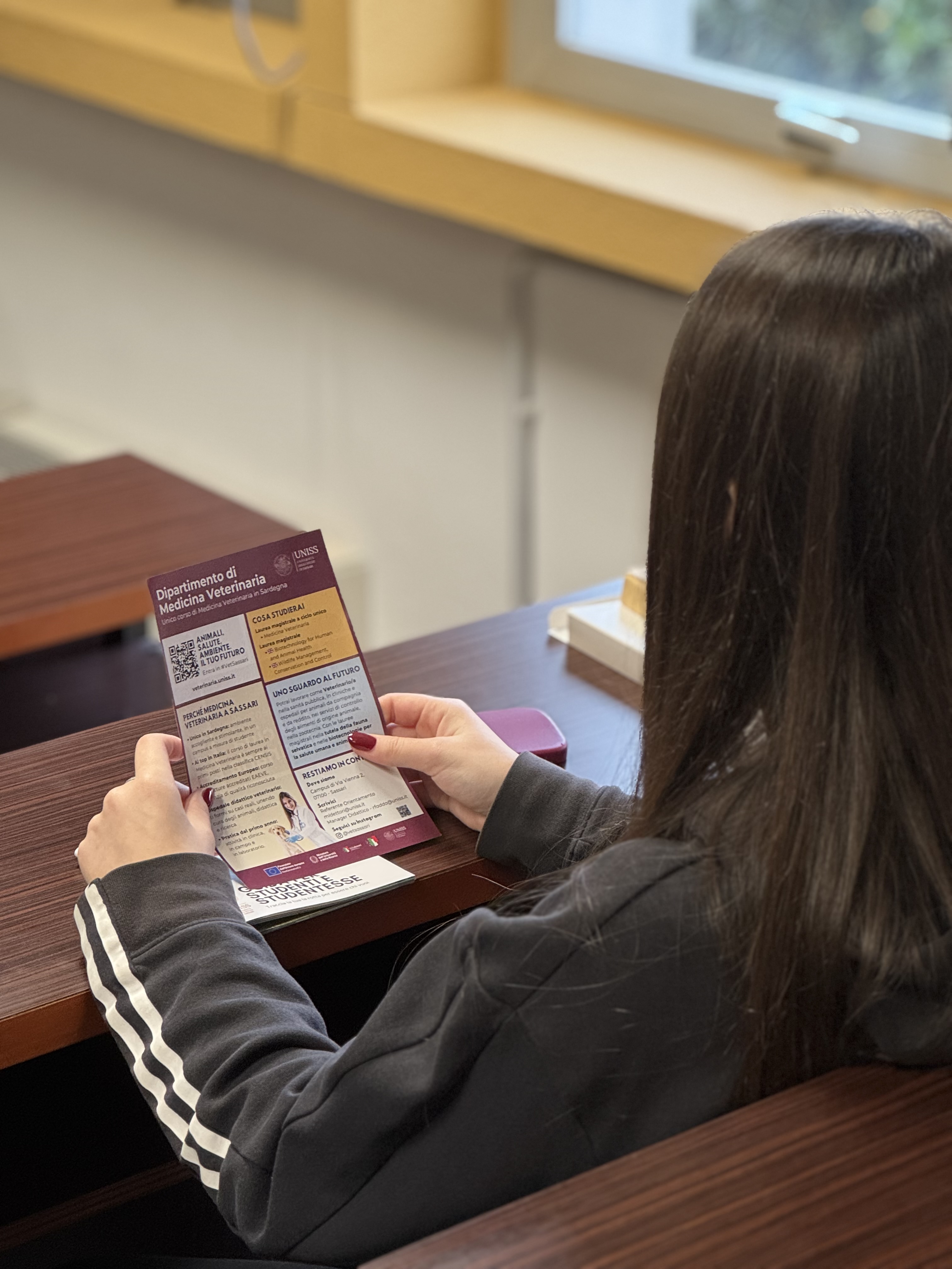 Studentessa in aula universitaria che consulta brochure del Dipartimento di Medicina Veterinaria: orientamento e scelte per il futuro.