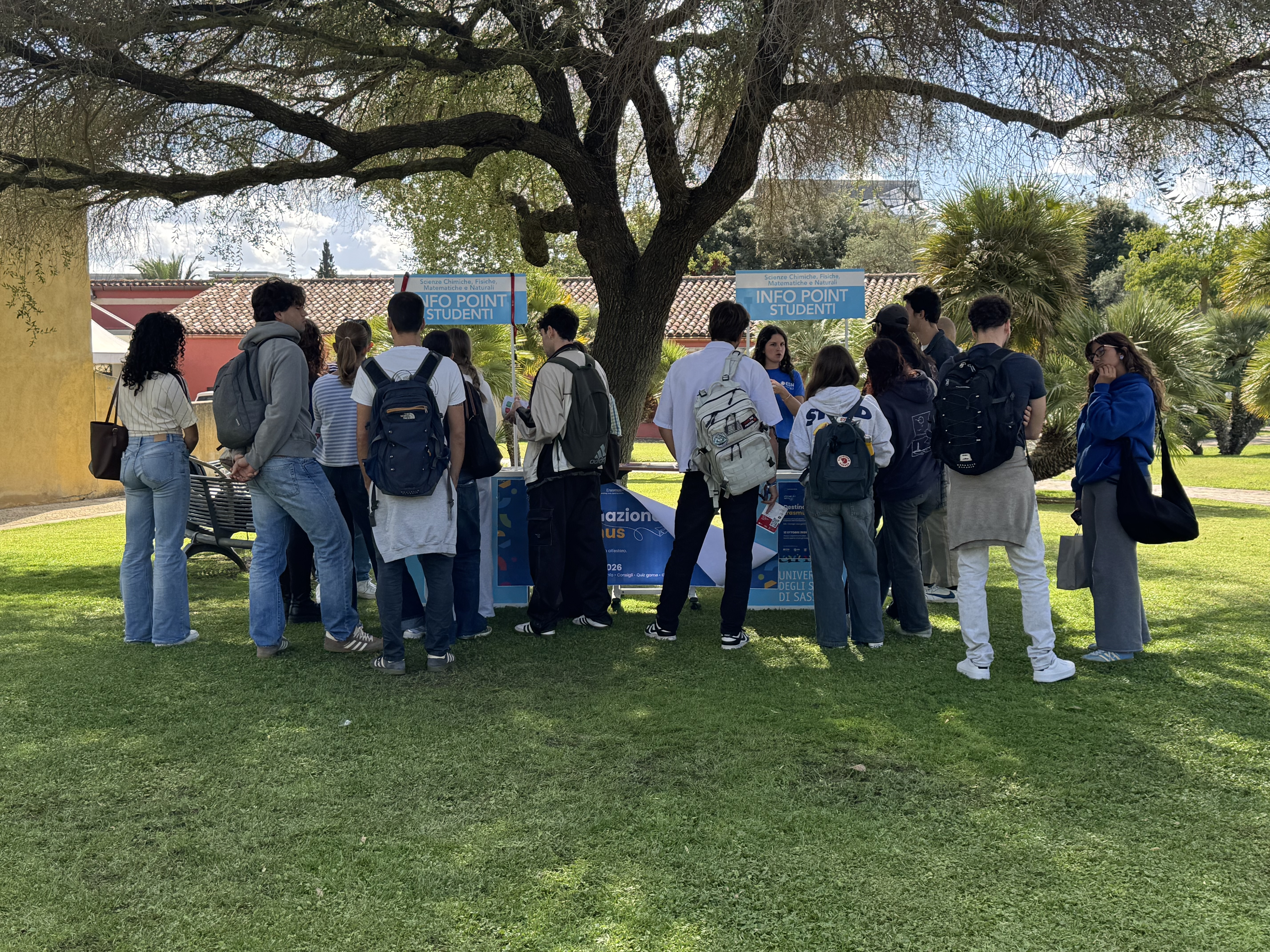 Panoramica dell'info point di Destinazione Erasmus, allestito nel giardino universitario con pannelli informativi, materiale promozionale e partecipanti.