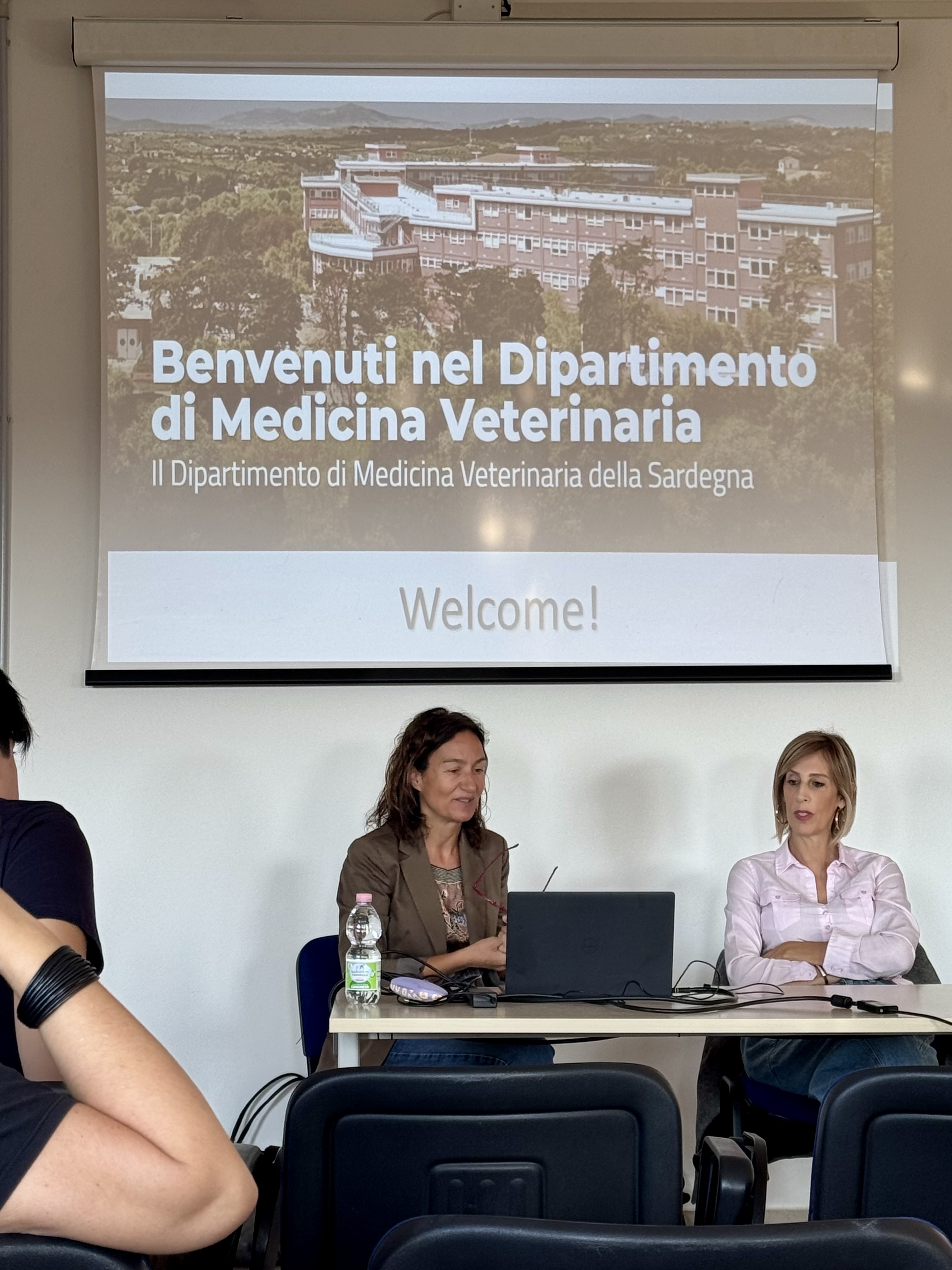 Due relatrici sedute alla cattedra sotto una slide con una veduta del Dipartimento e le scritte «Benvenuti nel Dipartimento di Medicina Veterinaria» e «Welcome!».